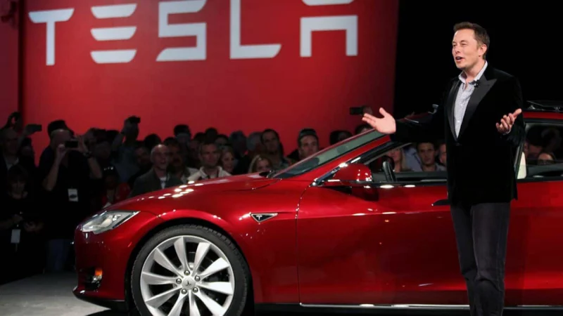 Photo of an incompetent moron standing in front of a red Tesla