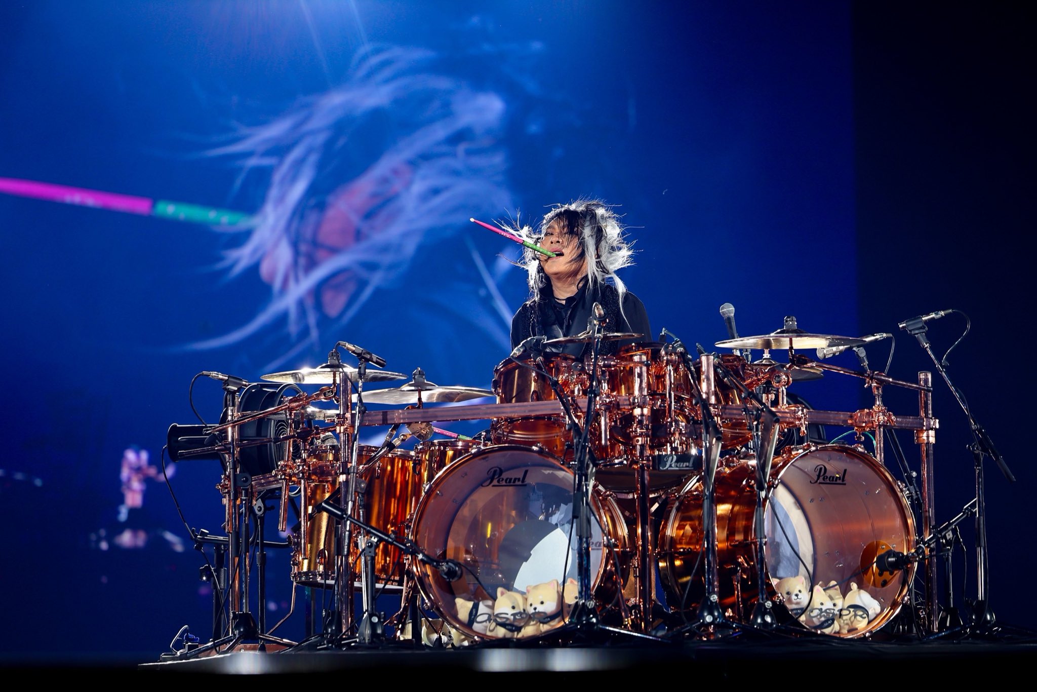 LUNA SEA's drummer Shinya (who recently passed away), behind his drum kit with a drum stick in his mouth.